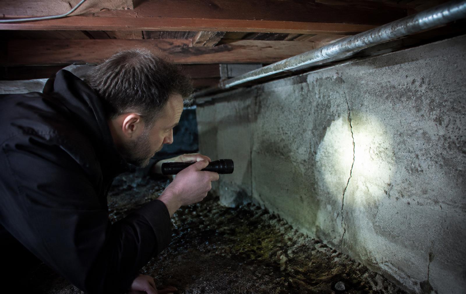Structural engineer inspecting a cracked foundation wall in the crawlspace of an older Seattle house