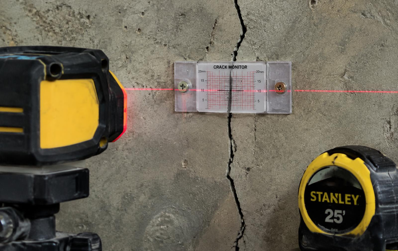 Crack monitor gauge and laser level on a concrete basement wall